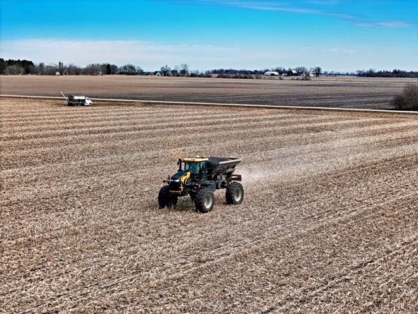 Self propelled spreader applying fertilizer to a field before tilling with farm scene in the distance